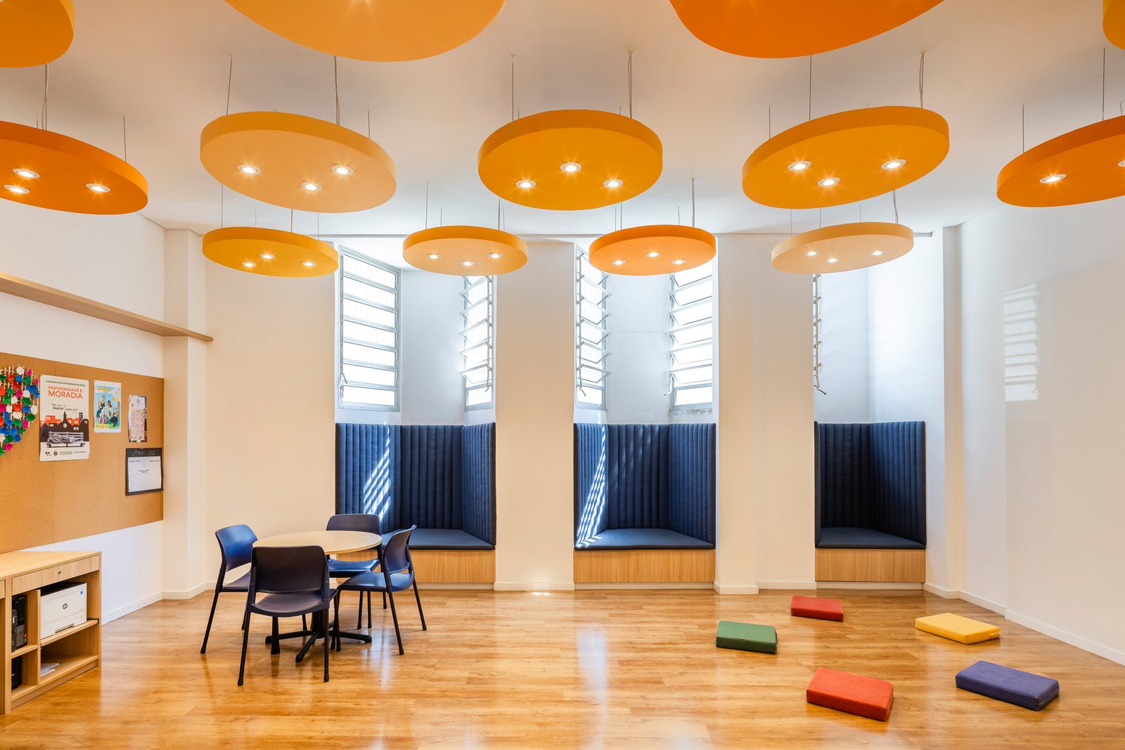 Sala da pastoral com luminárias suspensas em formato de nuvens laranja, nichos com bancos estofados azuis e almofadas coloridas no piso