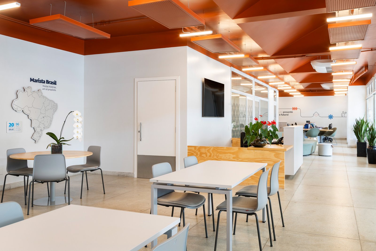 Área de coworking com mesas e mural Marista Brasil