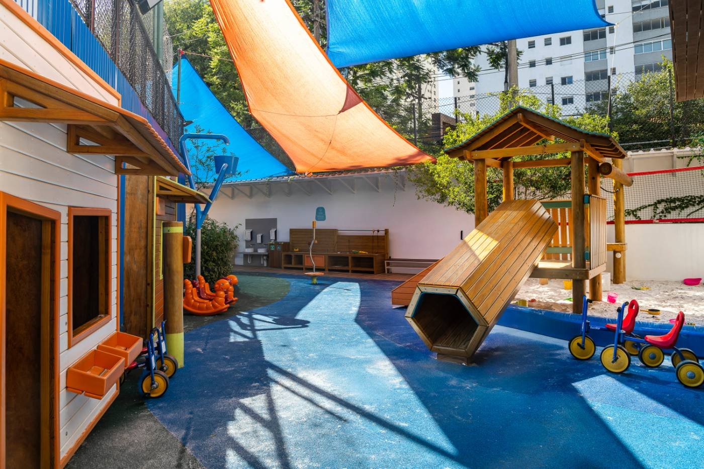 Parque em uso com piso azul, casinhas, escorregadores e velotróis