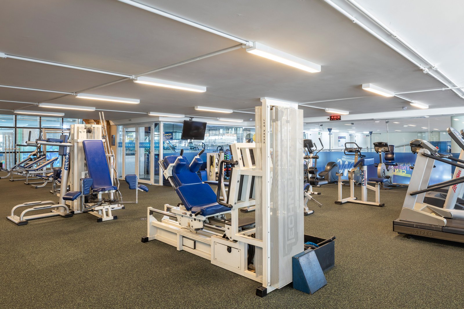 Sala de musculação entregue, com leg press, máquinas, esteiras e a fachada envidraçada voltada para as quadras