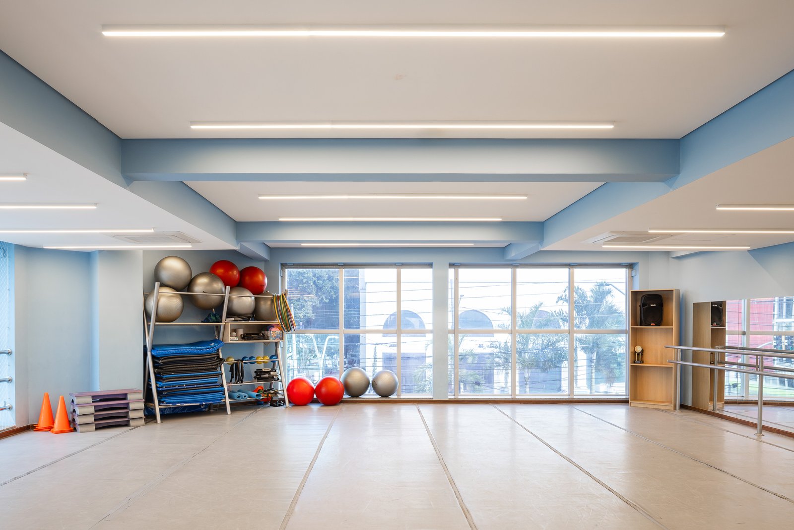 Sala de ginástica com forro e luminárias lineares, materiais organizados e vista para a rua