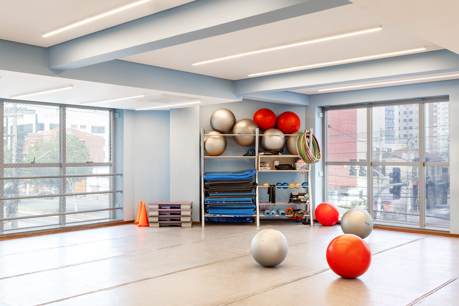 Sala de ginástica com bolas, colchonetes e nichos de organização junto às janelas