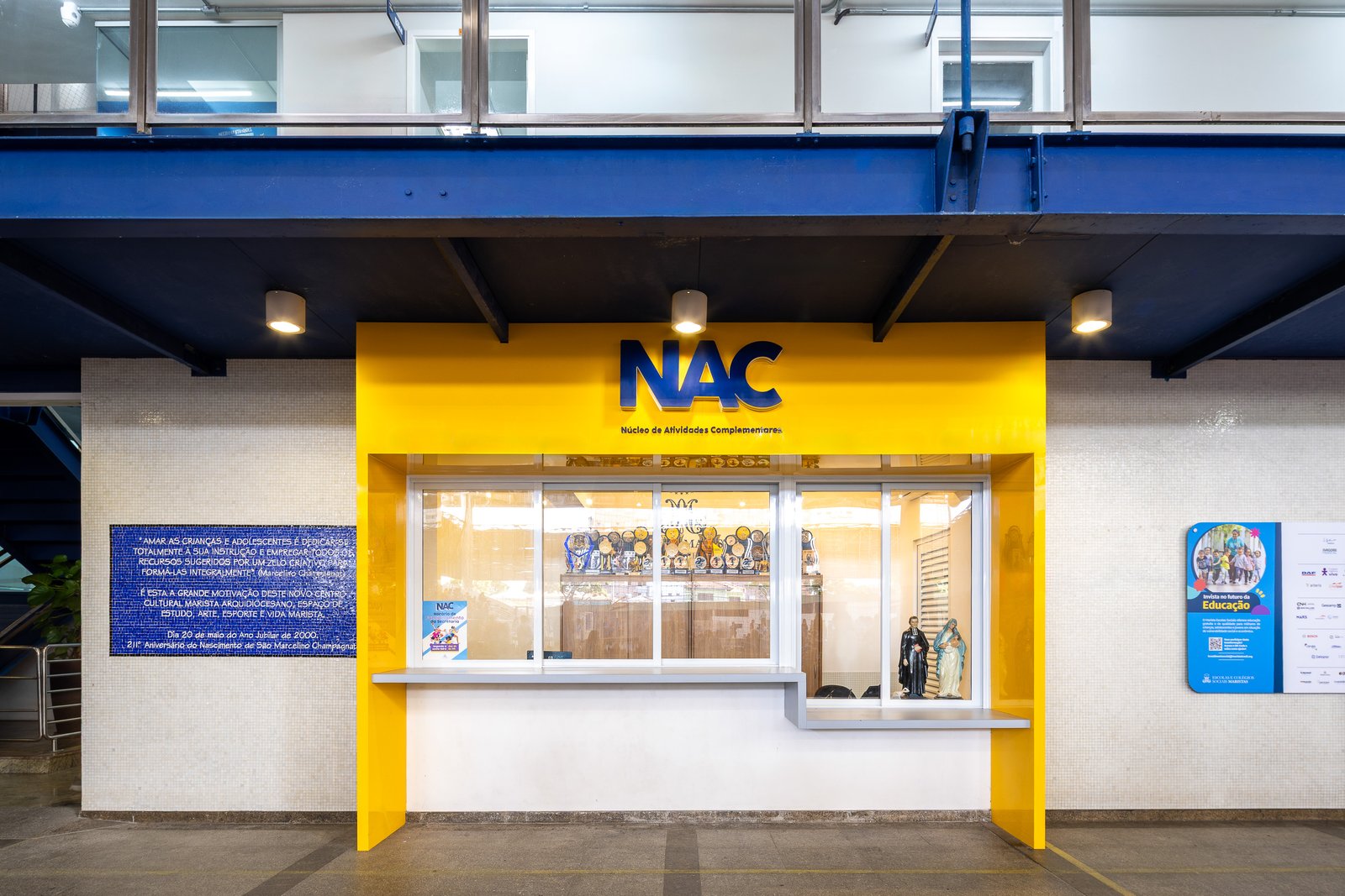 A nova fachada do NAC, com identidade visual em amarelo e azul, letreiro Núcleo de Atividades Complementares e vitrine de troféus