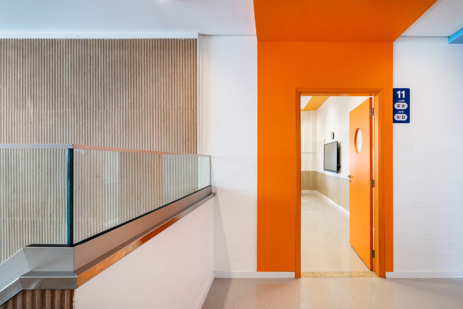 Corredor com porta azul de visor circular e placa de numeração