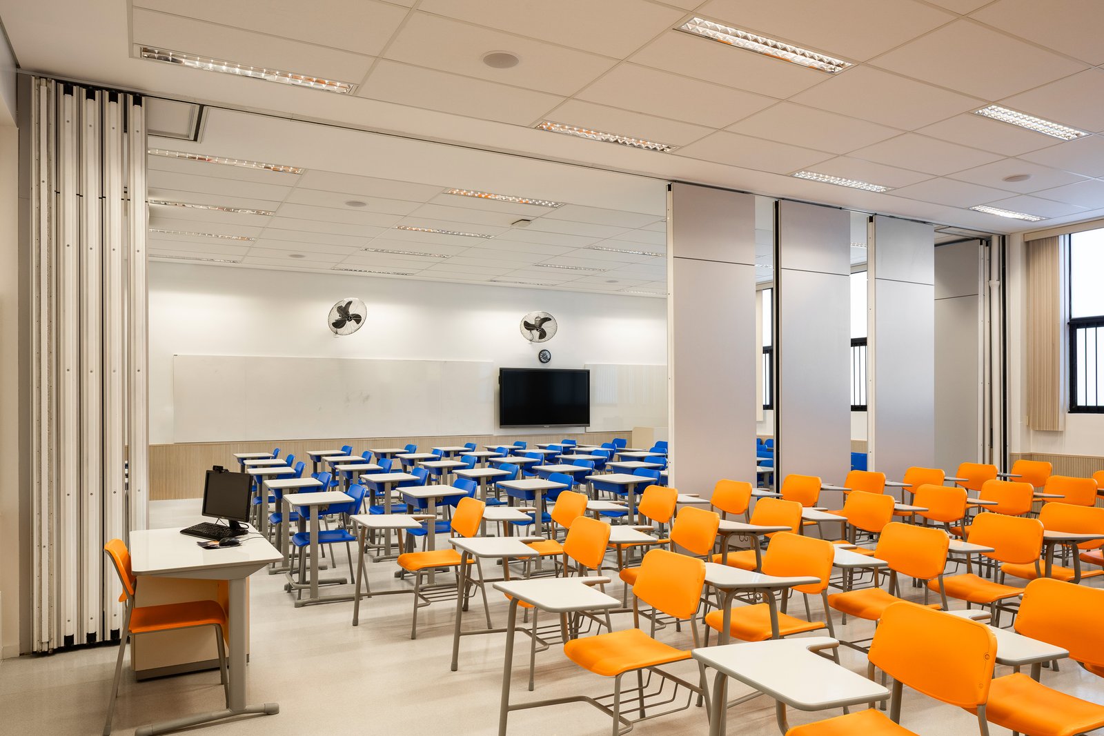 Sala de aula renovada com forro branco, friso laranja no teto, carteiras e cadeiras azuis