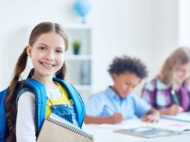 Smiling little scholar with rucksack and notepads on background of schoolboys