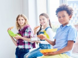 Adorable school learners with containers eating sandwiches on windowsill