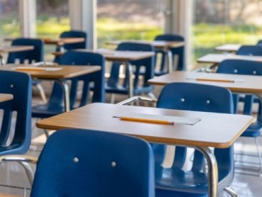 O que é arquitetura escolar em uma sala de aula organizada, com carteiras azuis, mesas com folhas e lápis e boa entrada de luz natural.