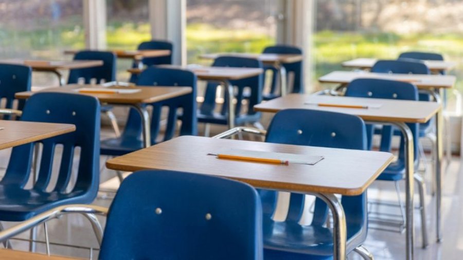 O que é arquitetura escolar em uma sala de aula organizada, com carteiras azuis, mesas com folhas e lápis e boa entrada de luz natural.