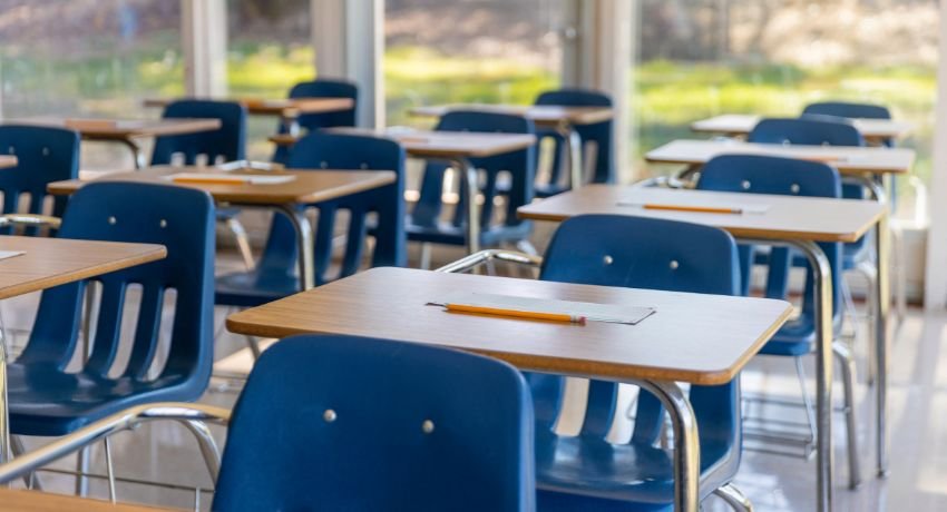O que é arquitetura escolar em uma sala de aula organizada, com carteiras azuis, mesas com folhas e lápis e boa entrada de luz natural.